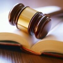 brown gavel and open book on a wooden table of the law in the courtroom